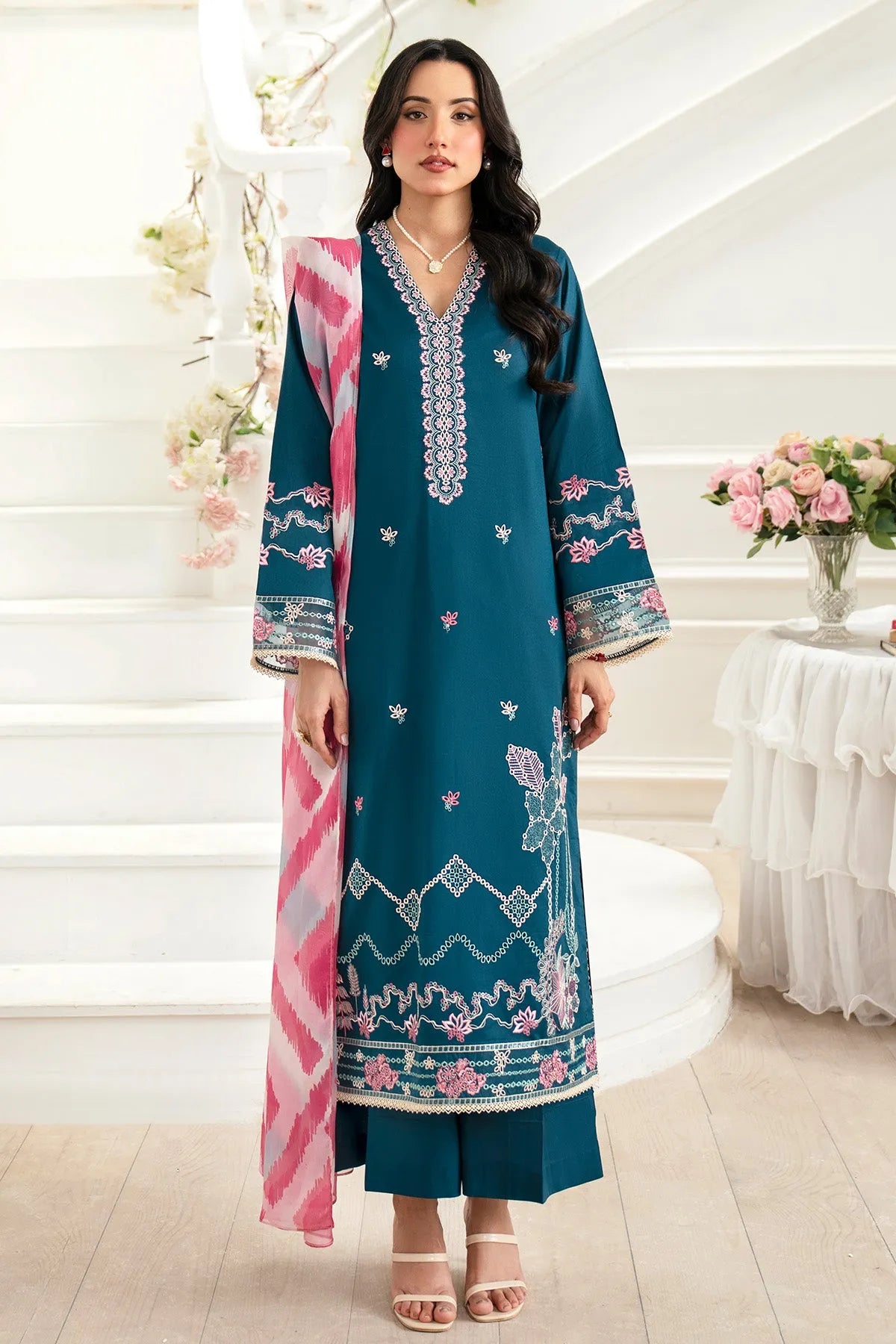 Woman wearing a teal and pink embroidered outfit in a decorated room.