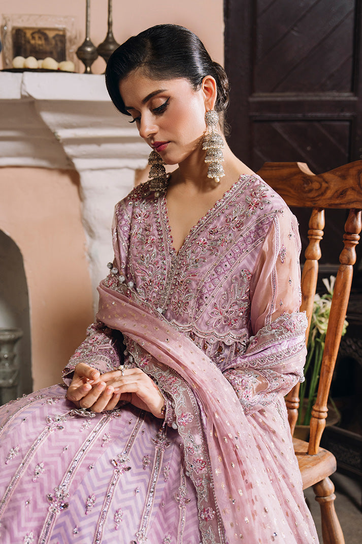 Seated model wearing a soft lilac-pink Nikkah dress with intricate silver and pink embroidery, embellished neckline and sleeves, and a matching sheer dupatta.
