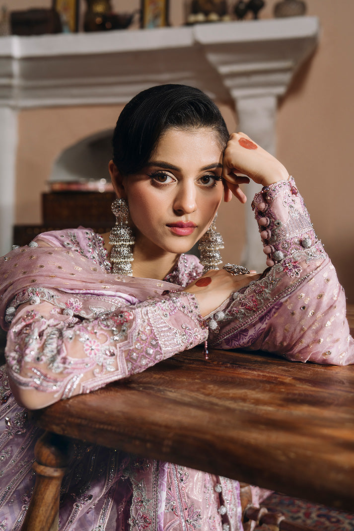 Close-up portrait of a model wearing a soft lilac-pink Nikkah dress with heavily embellished sleeves, delicate silver and pink embroidery, a matching dupatta, and statement silver earrings.