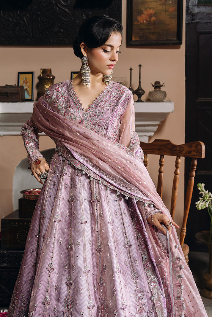 Front view of a model wearing a soft lilac-pink Nikkah dress with intricate silver and pink embroidery, a heavily embellished V-neck bodice, sheer sleeves, a flared embroidered skirt, and a matching embellished dupatta.