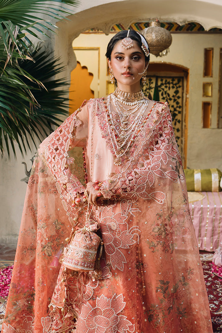 Front view of a peach pink Nikkah dress featuring intricate floral embroidery, an embellished sheer dupatta, layered bridal jewelry and a matching embroidered potli bag.
