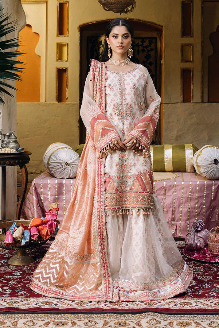 Model wearing an ivory Nikkah dress with peach floral embroidery, embellished sheer sleeves, flared sharara trousers, and a peach dupatta with detailed embroidered borders.