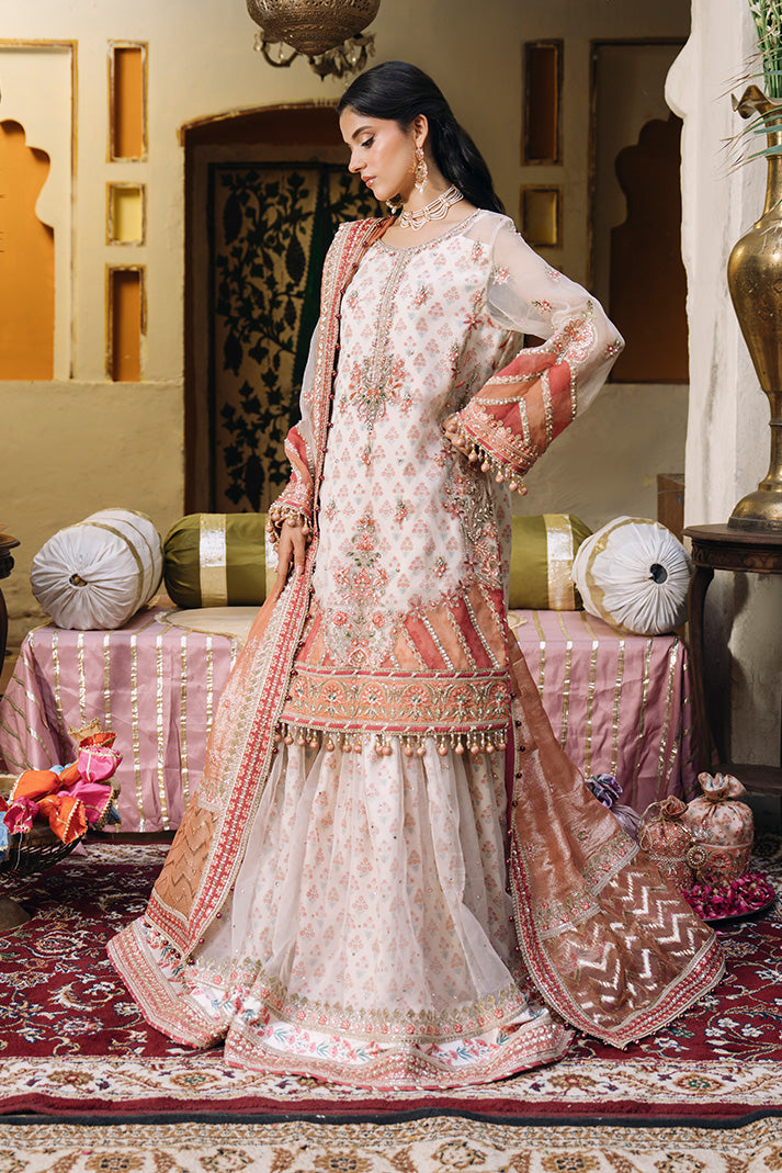 Model wearing an ivory Nikkah dress with delicate peach floral motifs, embellished sheer sleeves, flared sharara trousers, and a peach embroidered dupatta with ornate borders.