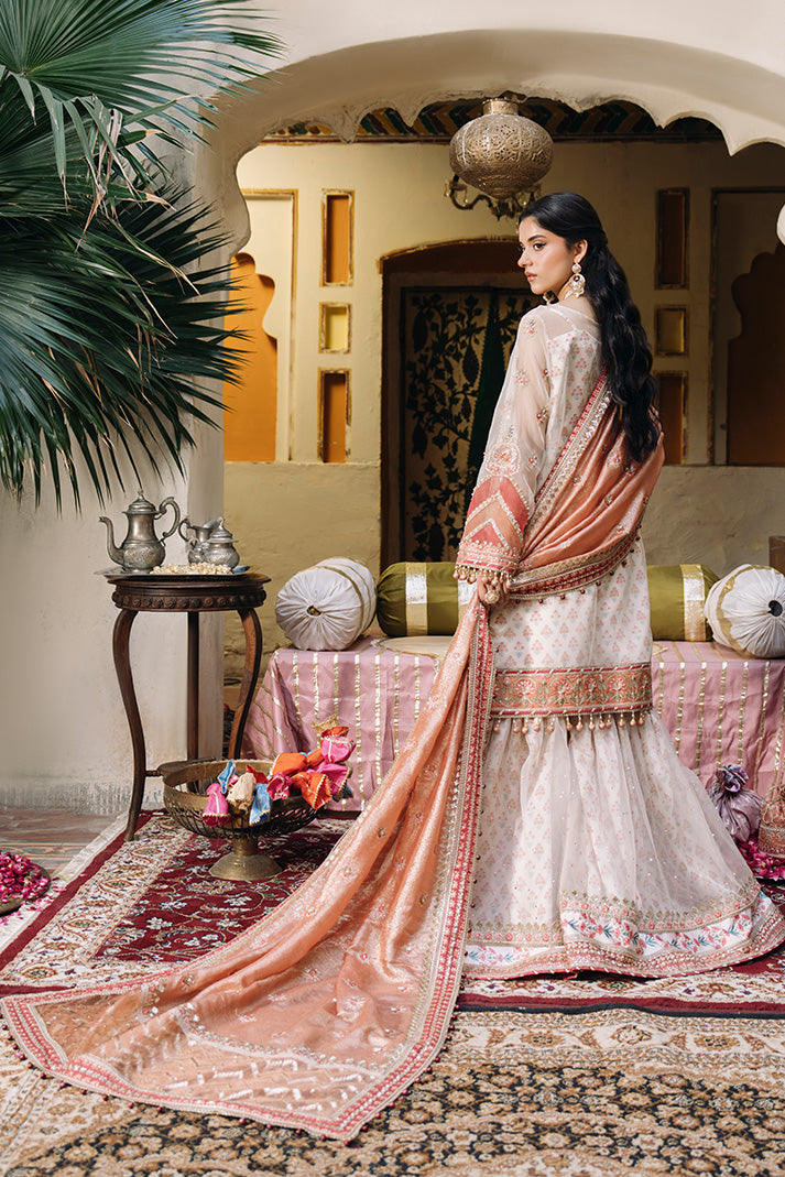 Model shown from the back wearing an ivory Nikkah dress with soft peach floral detailing, a flowing peach embroidered dupatta, and a wide embellished border with a long trailing drape.
