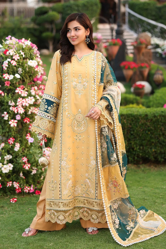 A woman posing in a traditional, mustard-colored unstitched three-piece shirt, dupatta, and trousers with embroidered details and organza borders, standing in a garden setting.