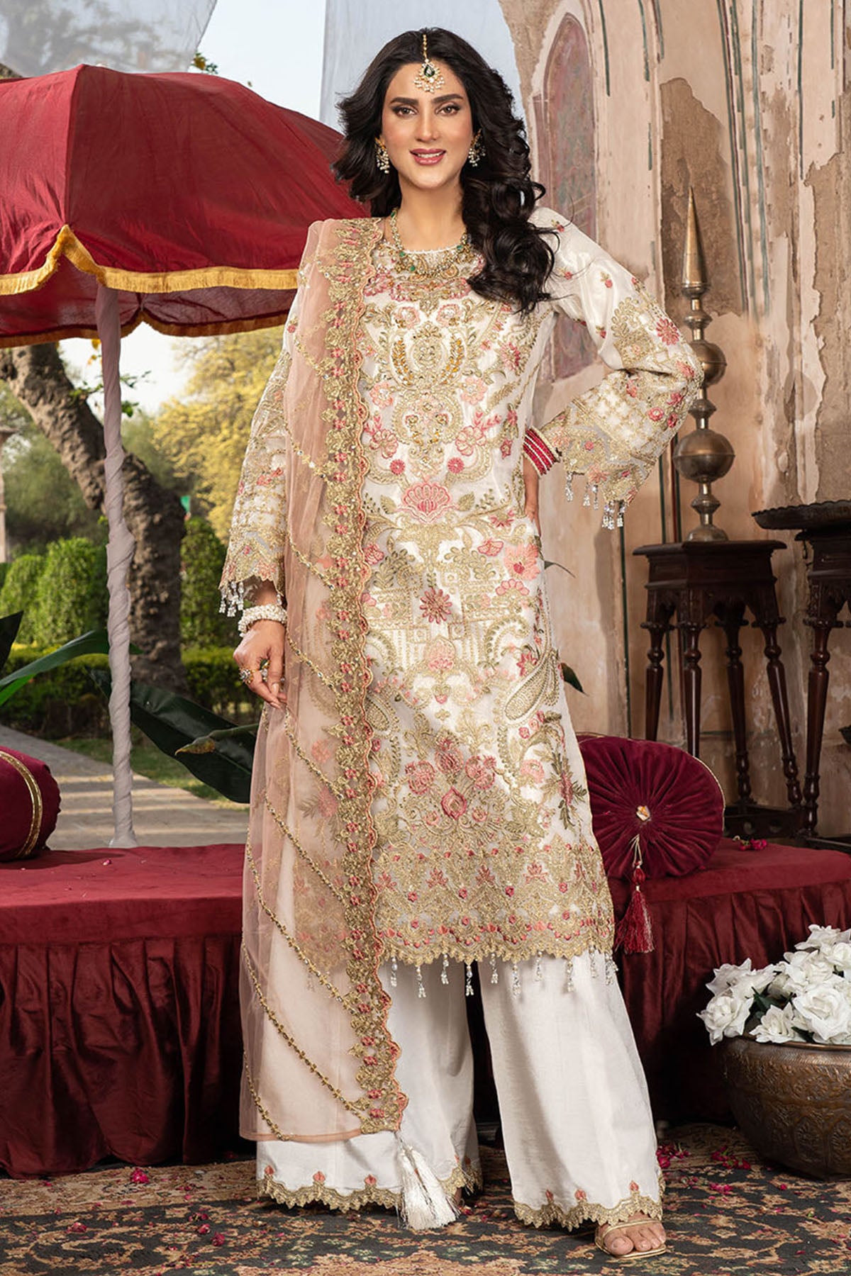 Woman in traditional embroidered outfit standing in an ornate indoor setting.
