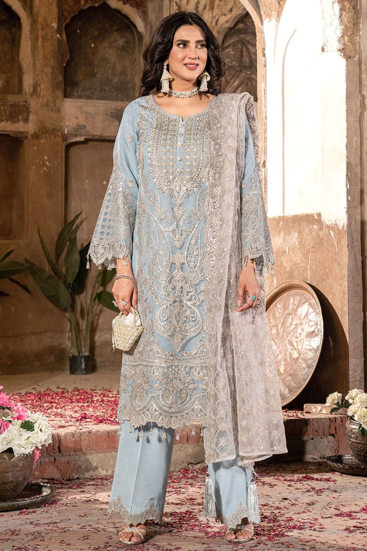 Woman in traditional embroidered outfit standing in an ornate indoor setting.